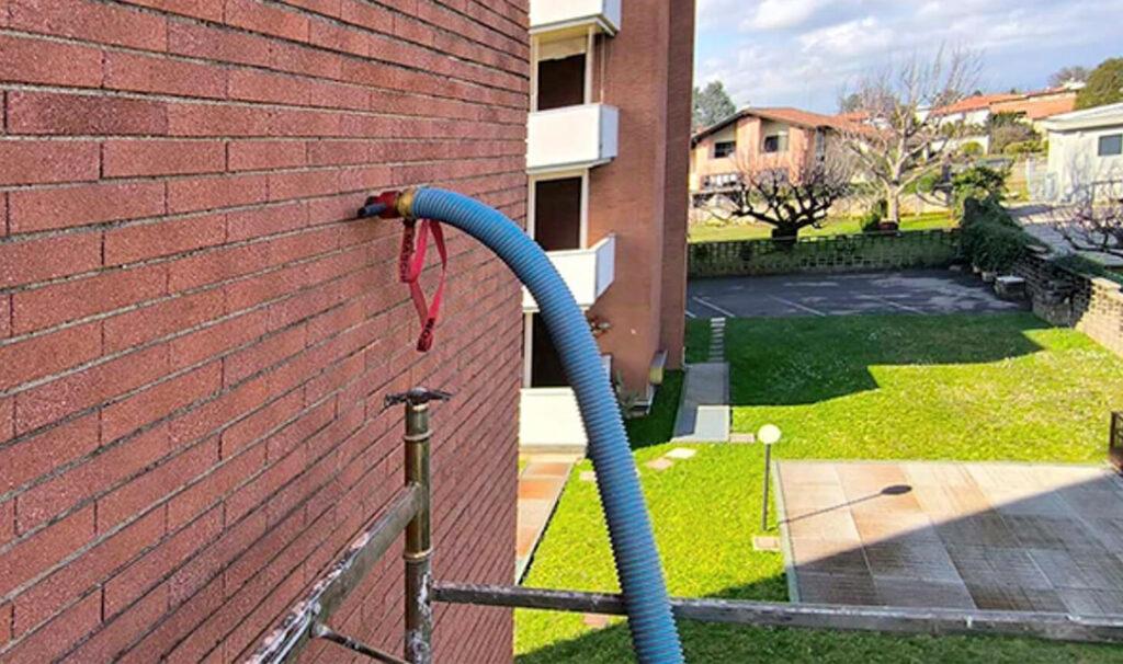 Manguera de insuflado introduciendo corcho natural en la cámara de aire de una fachada de ladrillo